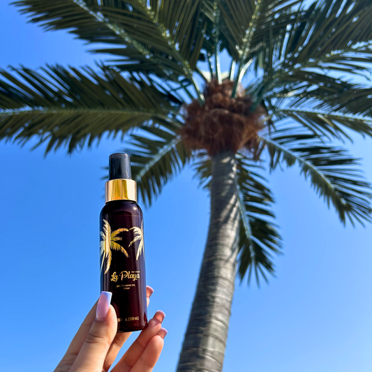 Osoba trzymająca butelkę La Playa na tropikalnej plaży z palmą w tle, podkreślając naturalne opalanie i egzotyczny klimat
