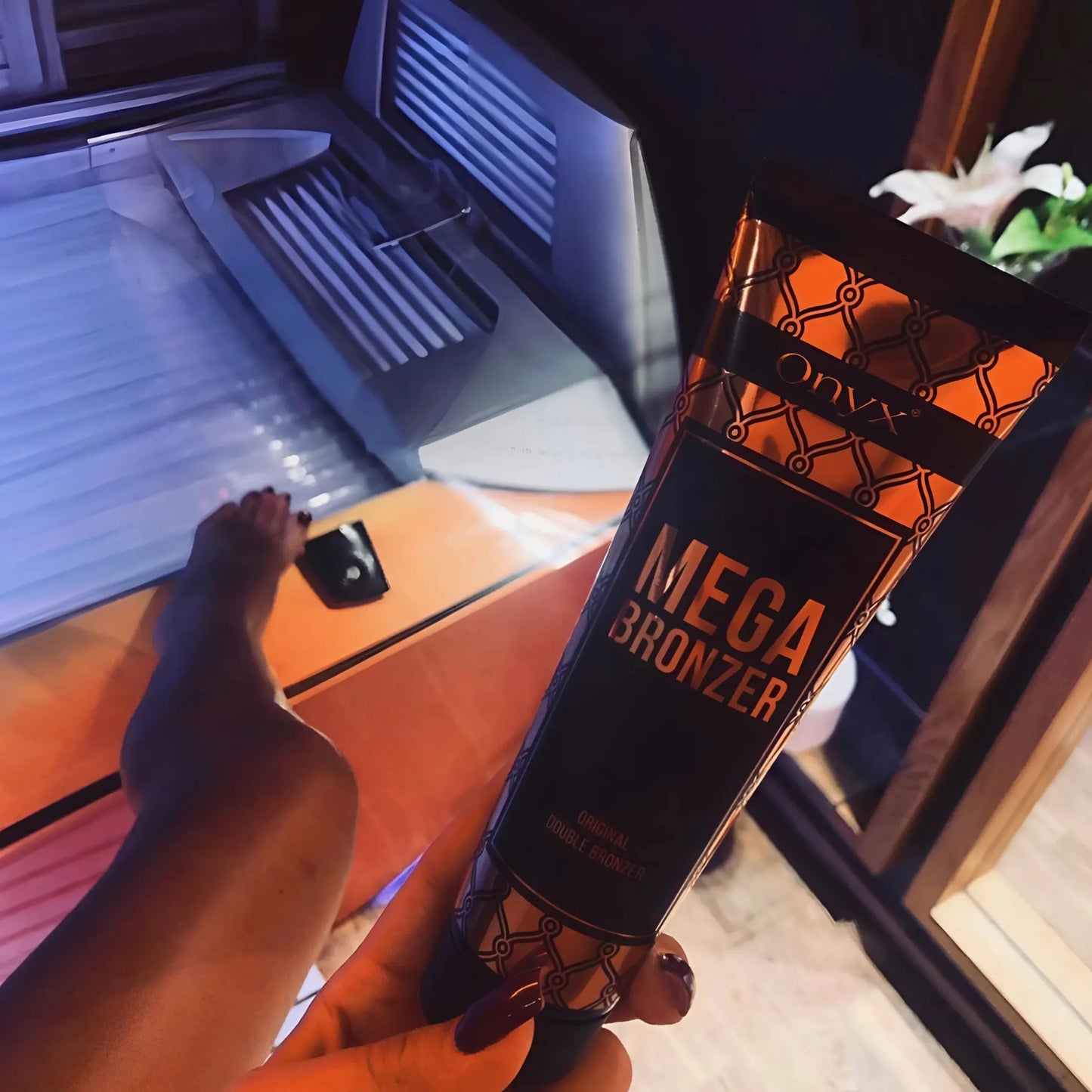 Ręka trzymająca tubę balsamu Onyx Mega Bronzer nad otwartym solarium, gotowa do nałożenia produktu przed sesją opalania