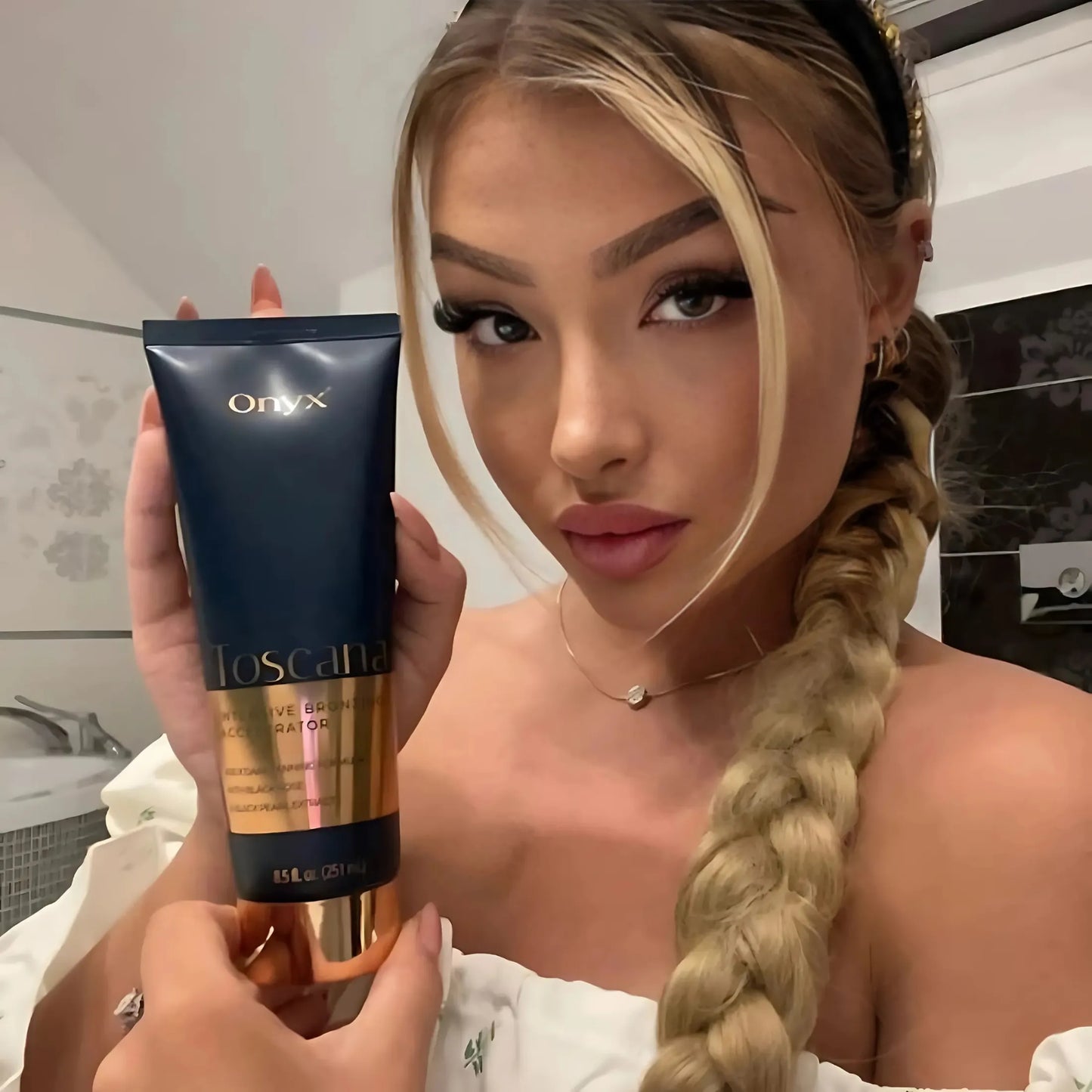 Kobieta z blond włosami i długim warkoczem trzyma balsam Onyx Toscana, delikatny makijaż i białe ubranie podkreślają elegancki wygląd